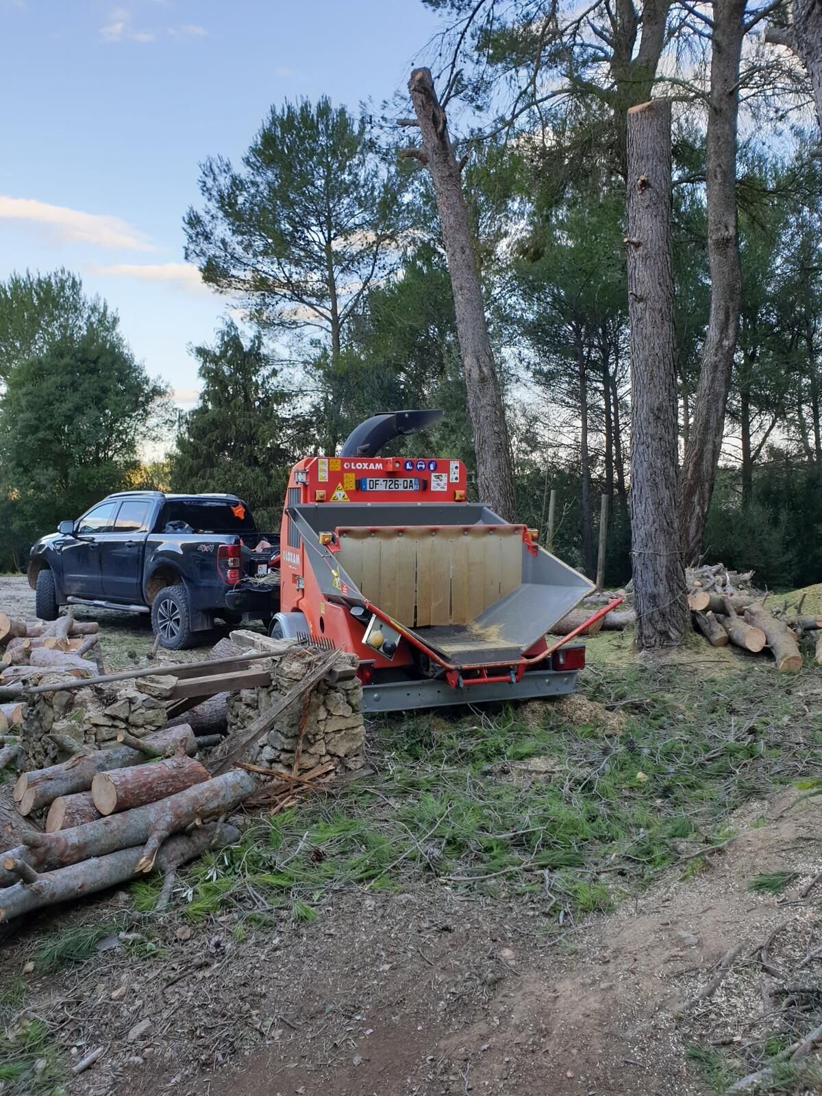 Broyeur de branches sur le chantier et bois bûché rangé en tas après abattage